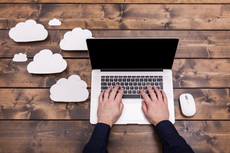 a Small Business Owner Typing on a Laptop with Cloud Symbols Floating Up from the Computer.